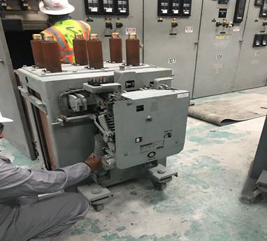 Worker inspecting gray electrical switchgear in an industrial control room.