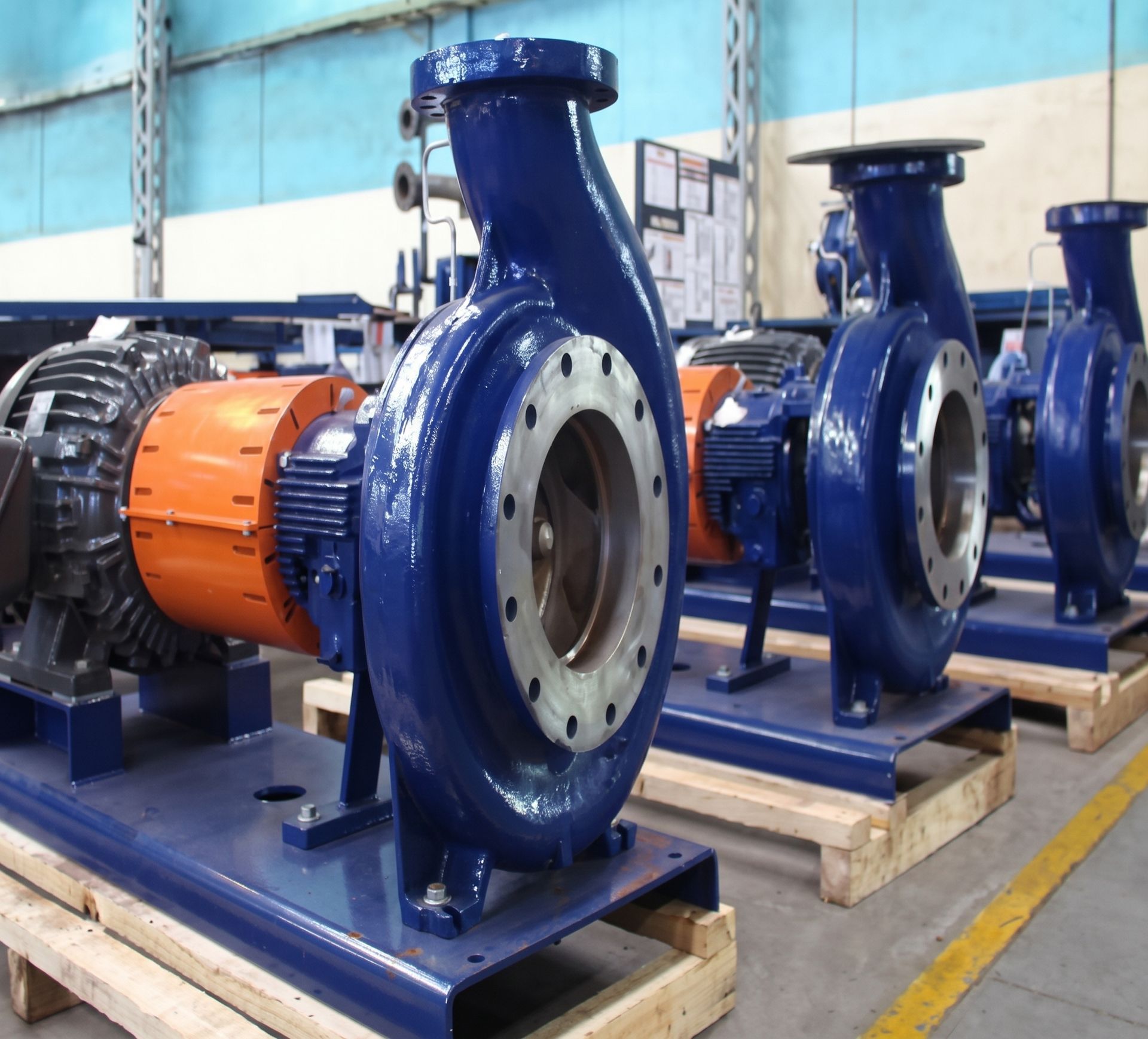 Blue industrial pumps and motors mounted on pallets in a factory warehouse.