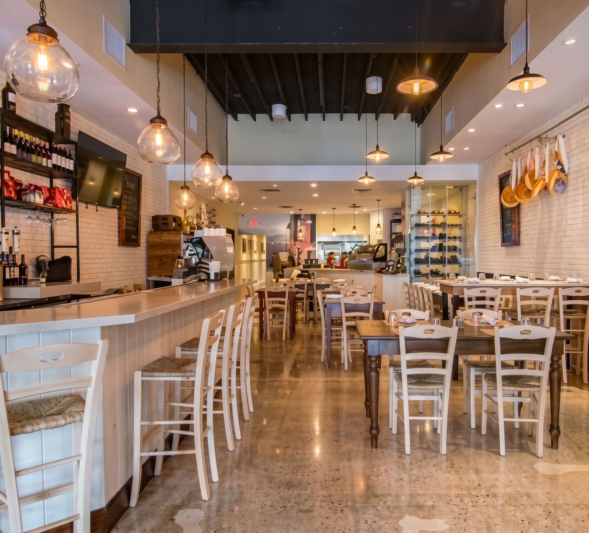 Bright, modern café interior with white chairs, wooden tables, pendant lights, and a long bar counter
