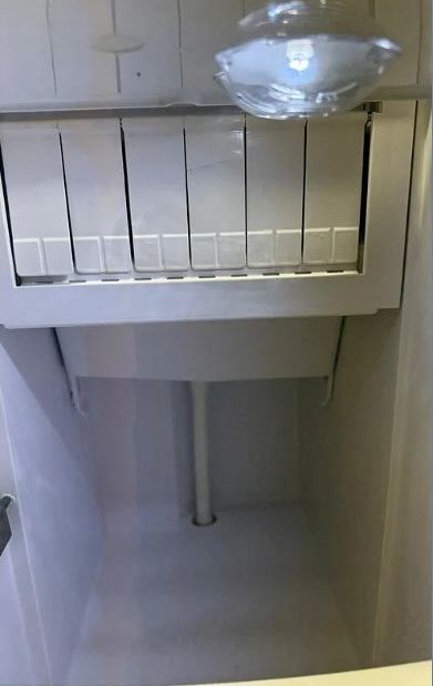 Empty white freezer compartment with wire shelves and a clear plastic container on the top shelf.