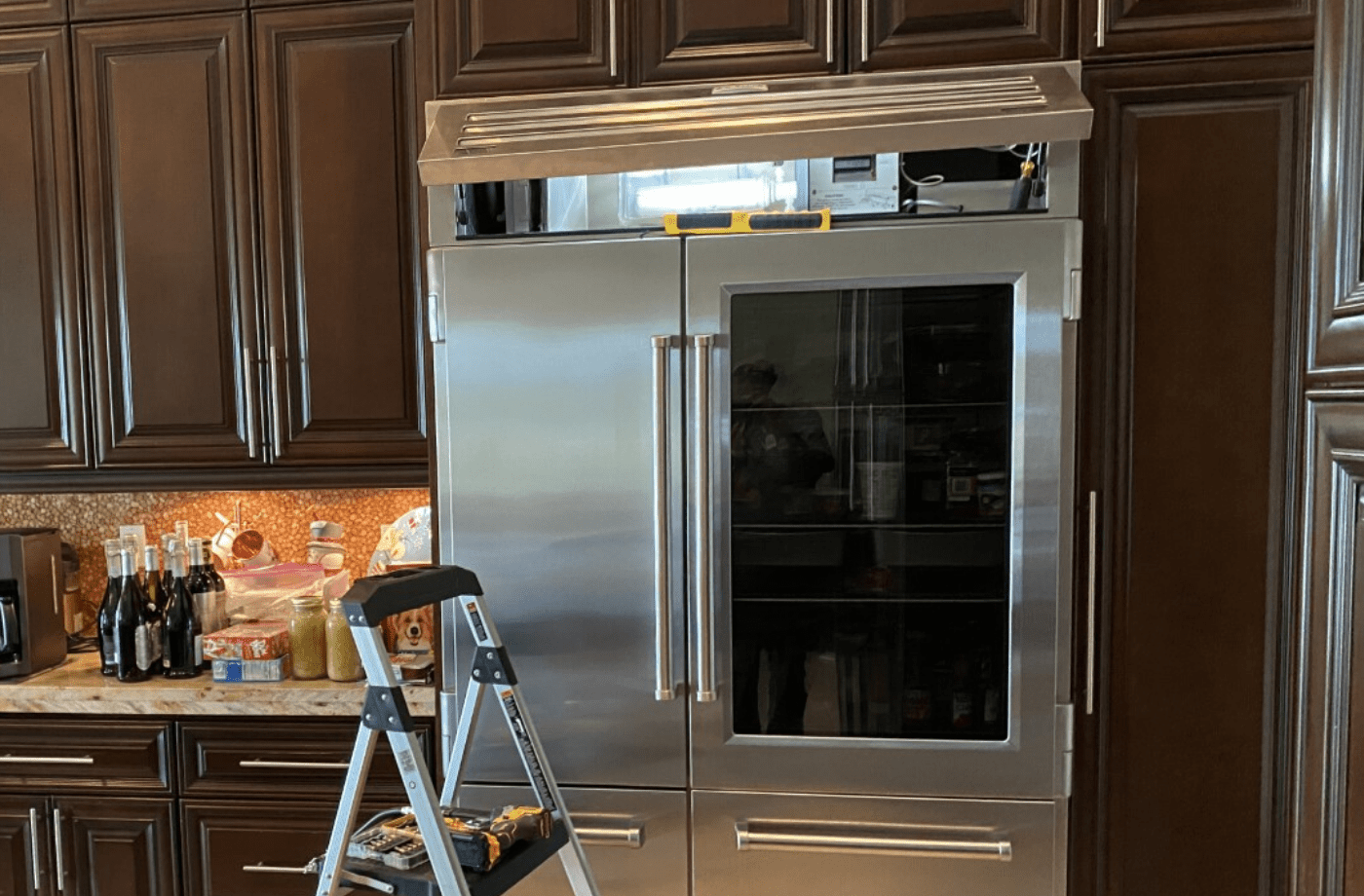Kitchen with a stainless steel built-in refrigerator and a step ladder in front of wooden cabinets.