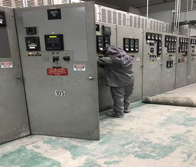 Worker inspecting electrical control panels in an industrial room