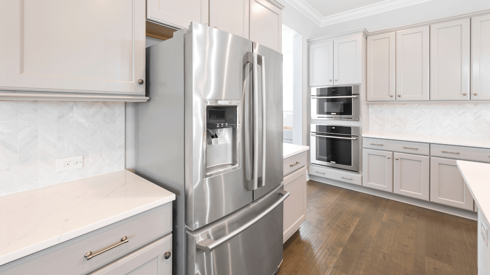Stainless steel refrigerator in a modern kitchen with white cabinets, countertops, and hardwood floors.