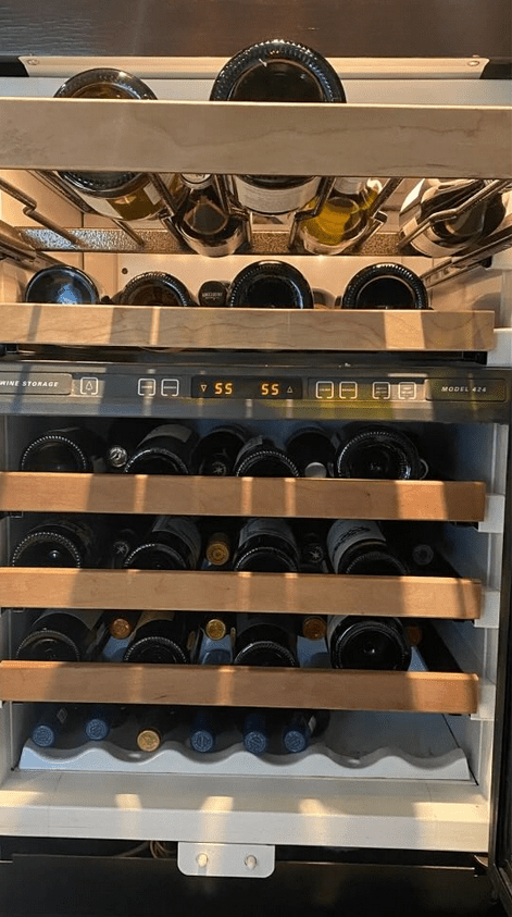 Wine bottles stored on metal racks in a glass-door wine cooler, with a digital temperature display.