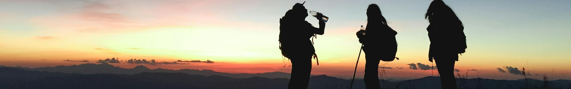Three silhouetted figures on a mountain at sunset.
