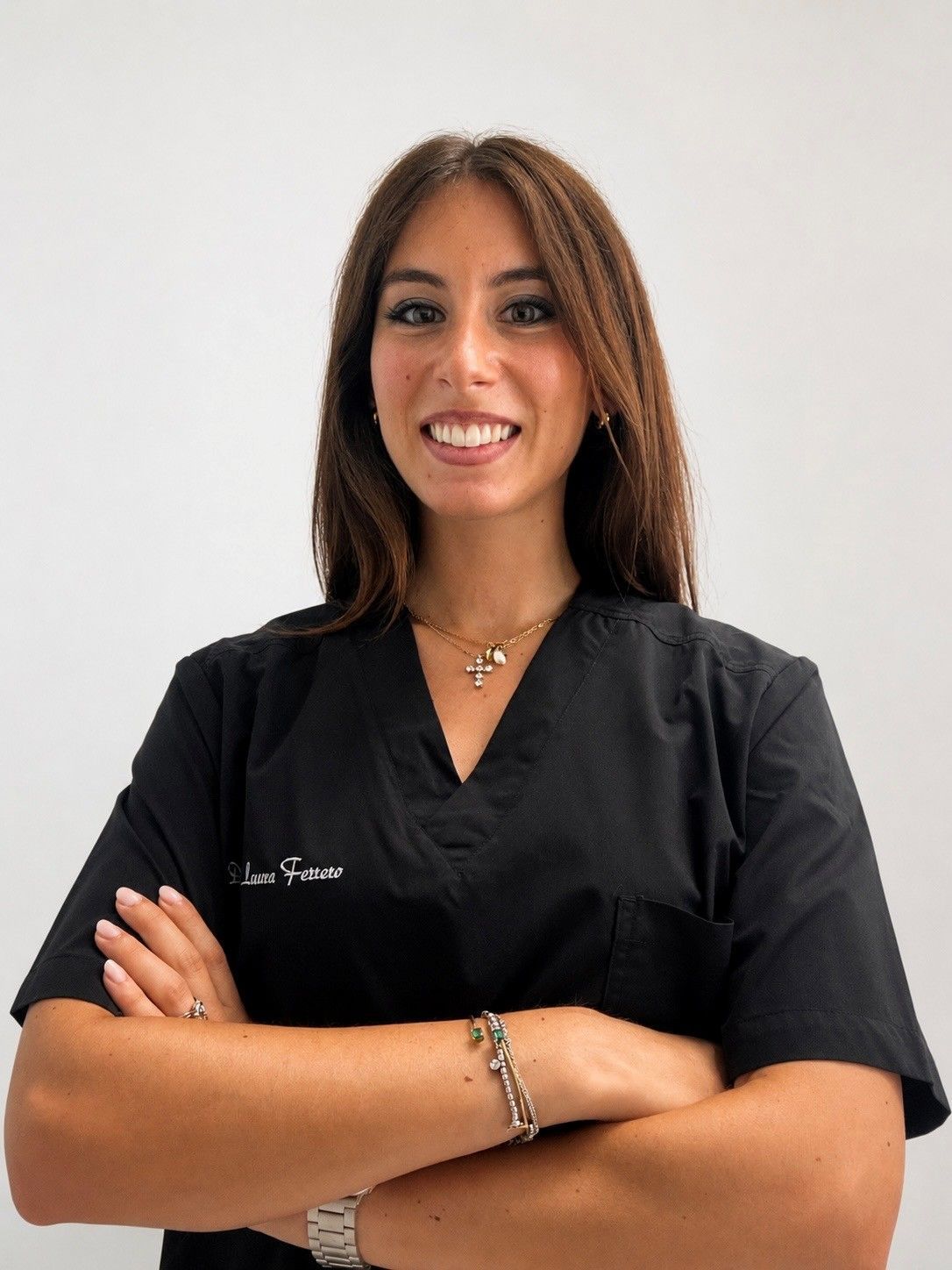 Donna sorridente in camice nero con le braccia incrociate su uno sfondo bianco uniforme