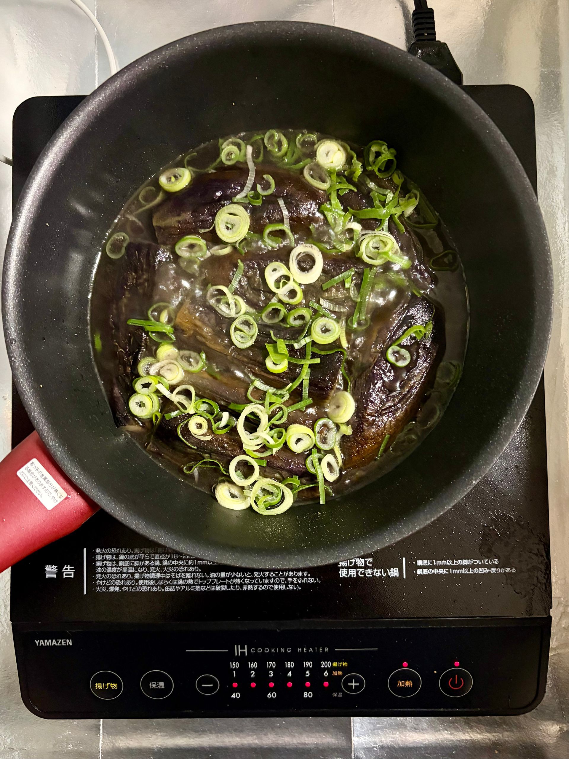 eggplant in frying pan with spring onions added