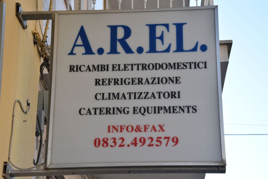 Cartello per i servizi di riparazione e refrigerazione di elettrodomestici AREL con numero di telefono rosso su sfondo bianco.
