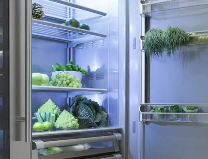 Frigorifero aperto, pieno di verdure fresche e erbe aromatiche su ripiani e scomparti sulla porta.