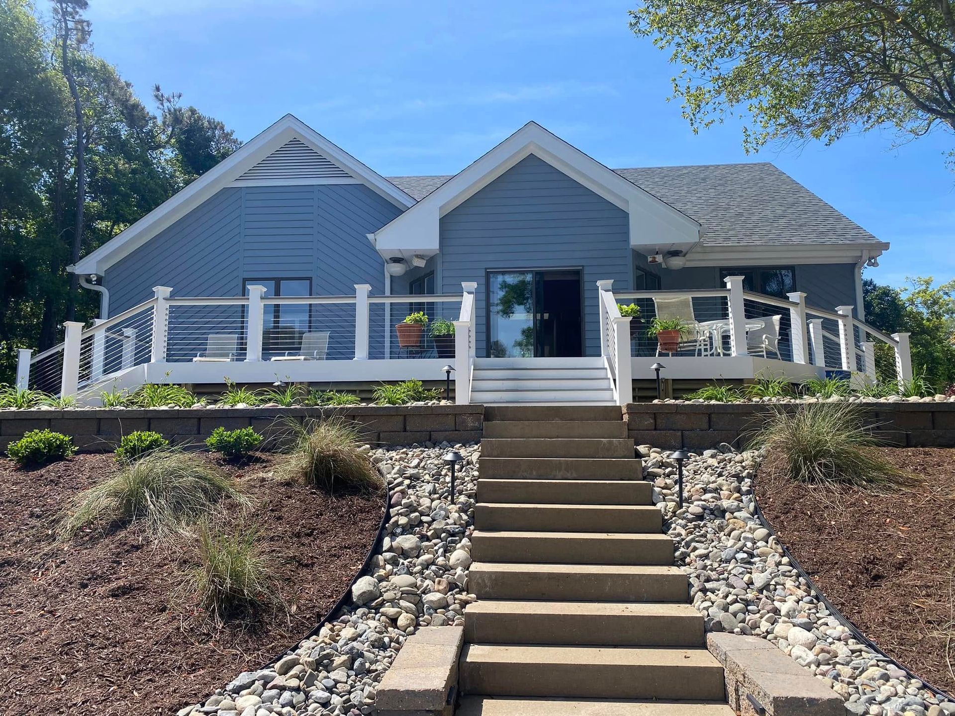 Blue house with a front porch, central steps, and stone landscaping on a sunny day