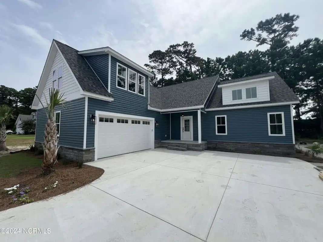 Blue-gray house with white trim and double garage on a concrete driveway, surrounded by trees