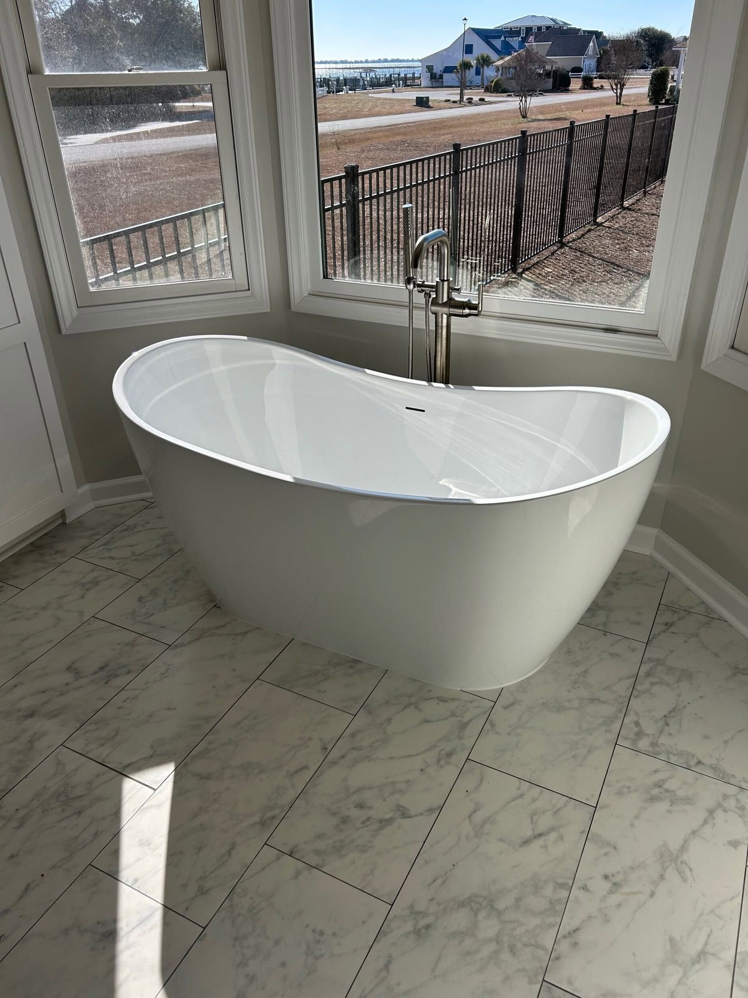 Freestanding white bathtub in a bright bathroom by large windows and a wood deck view