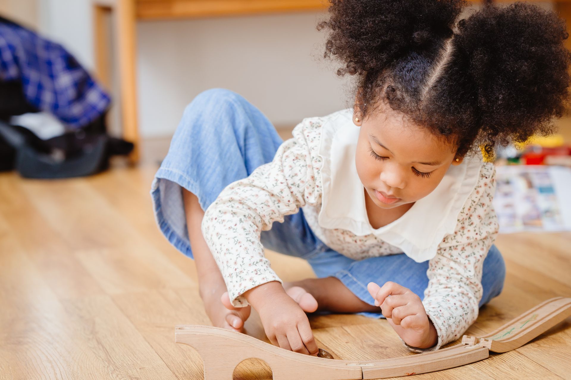 Child kneeling on a wooden floor, playing with a wooden puzzle board indoors.