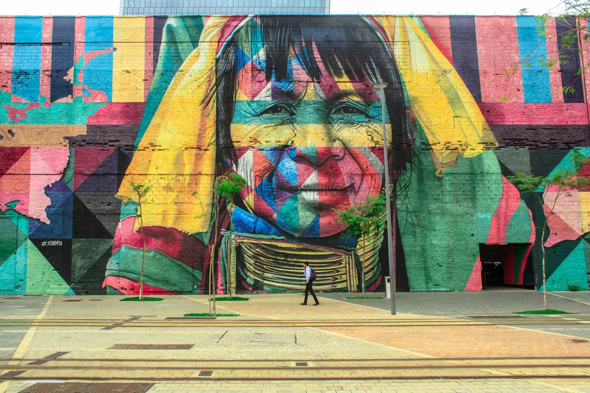 Colorful mural of a smiling face on a brick wall, with a lone person walking in front of it
