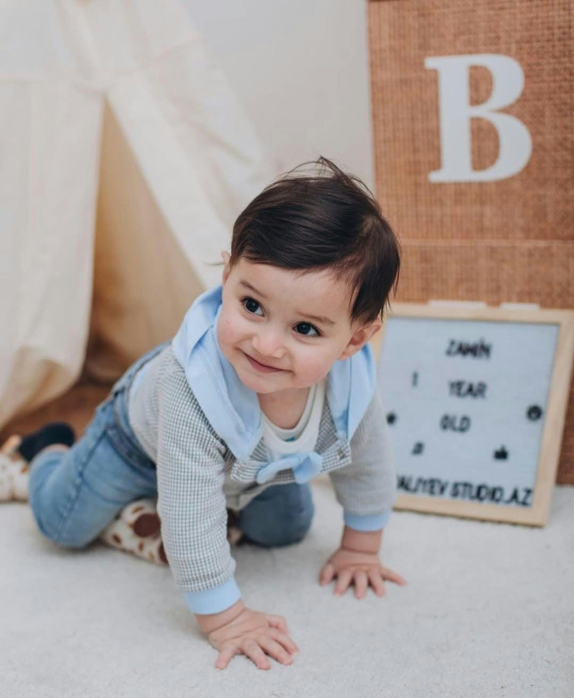 Baby crawling on a white rug beside a letter board and large wooden letter B.