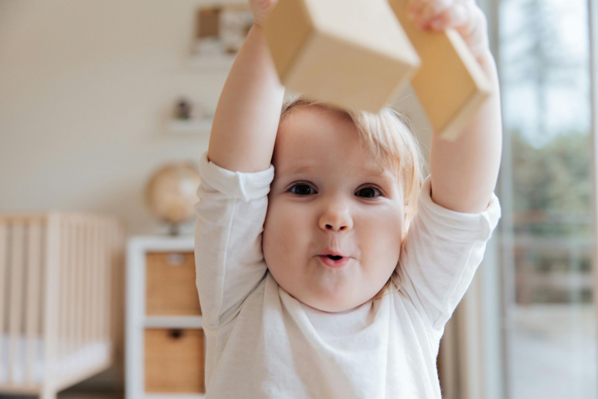 Child holding wooden blocks overhead in a bright room