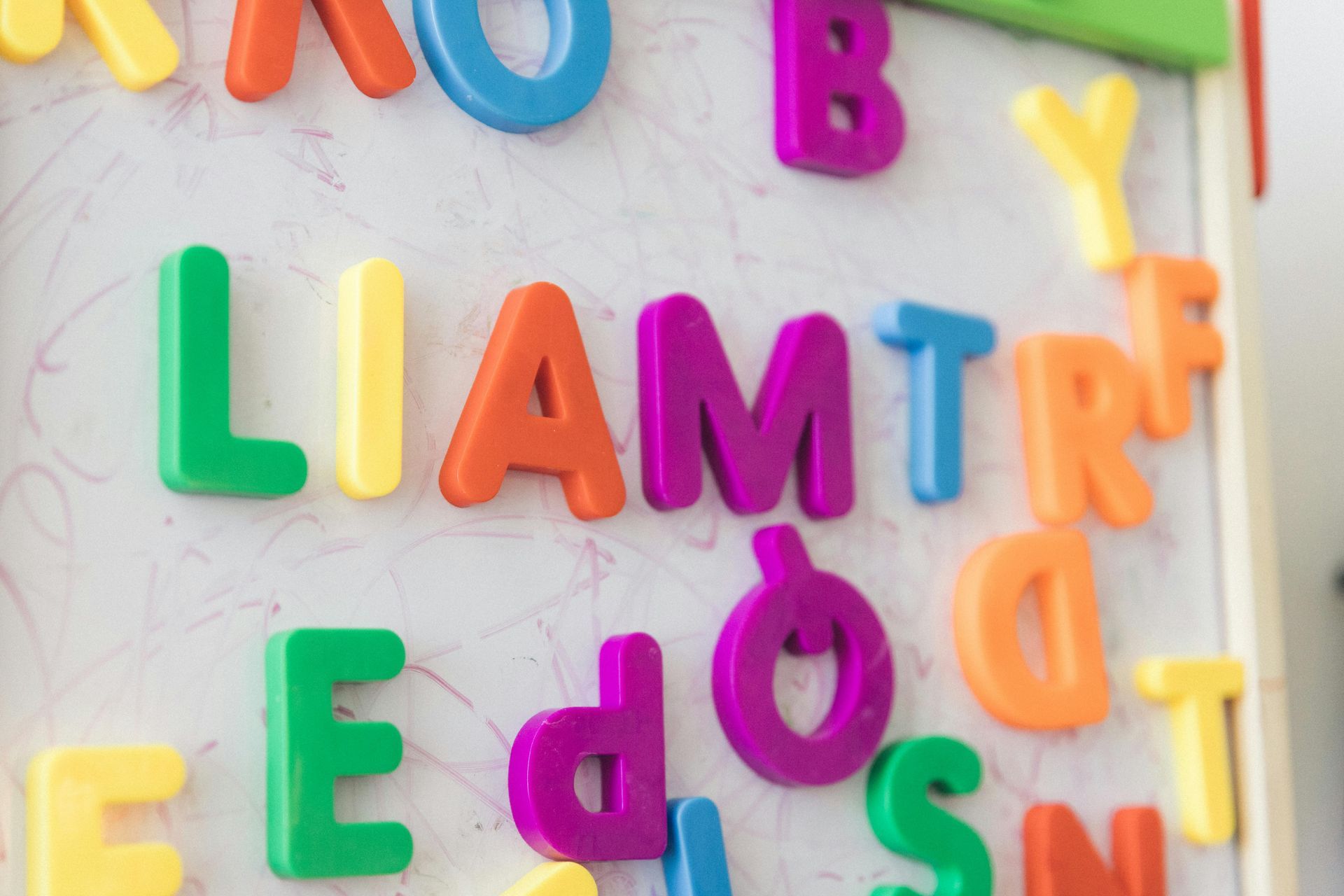 Colorful alphabet magnets on a whiteboard spelling “LIAM” and other scattered letters
