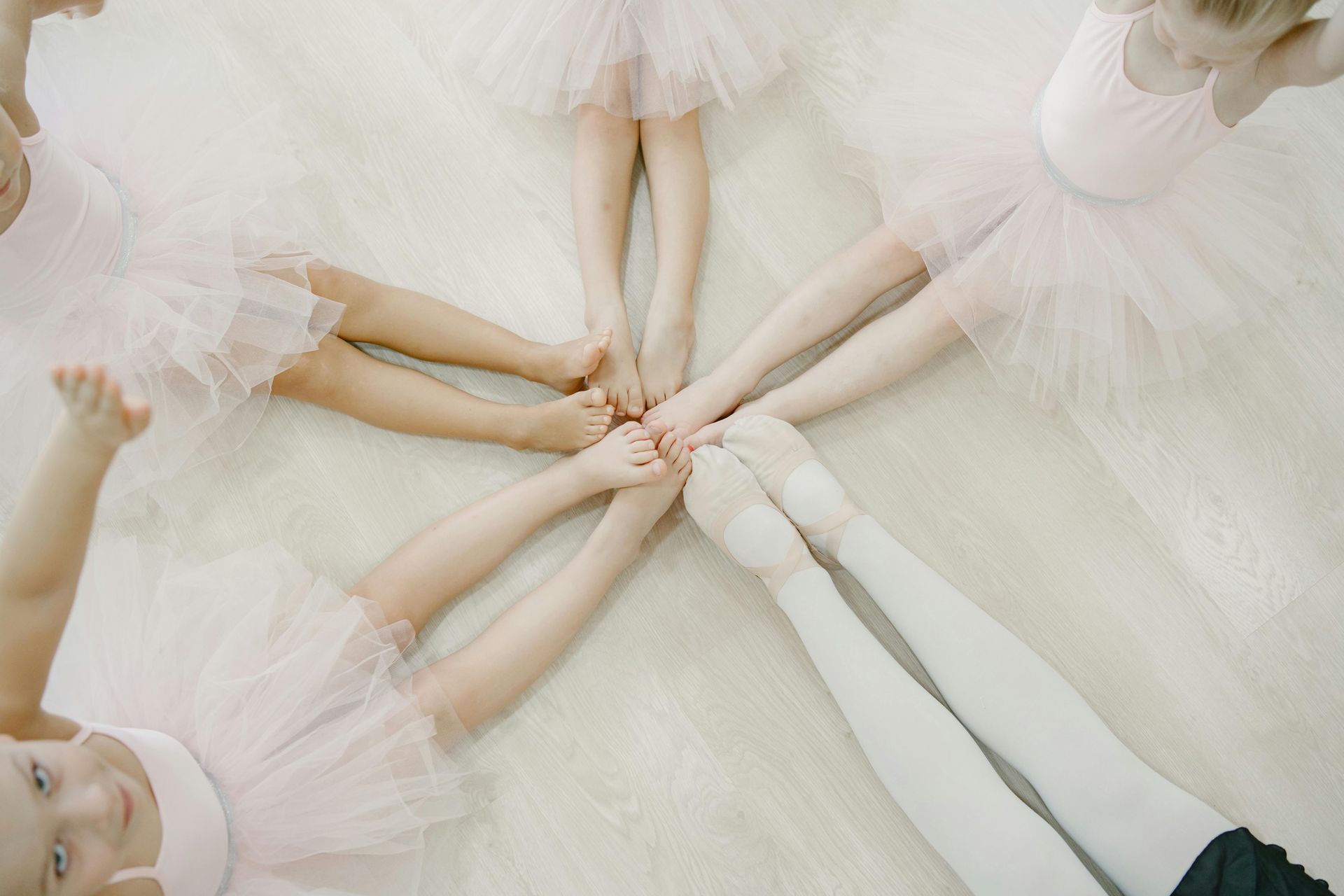 Ballet dancers’ hands and feet joined in a circle on a pale studio floor