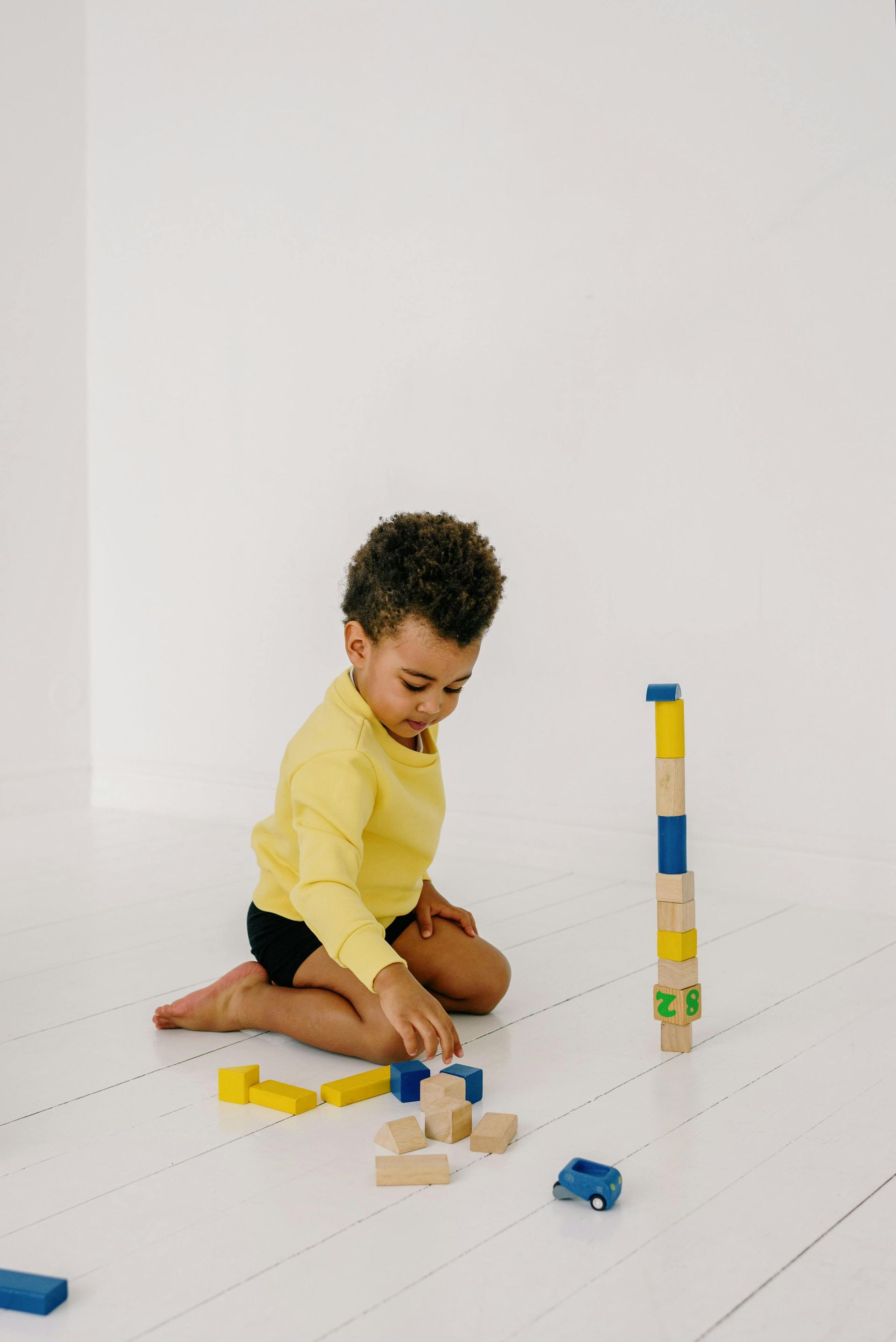 Child in yellow shirt building with colorful blocks on a white floor in a bright room
