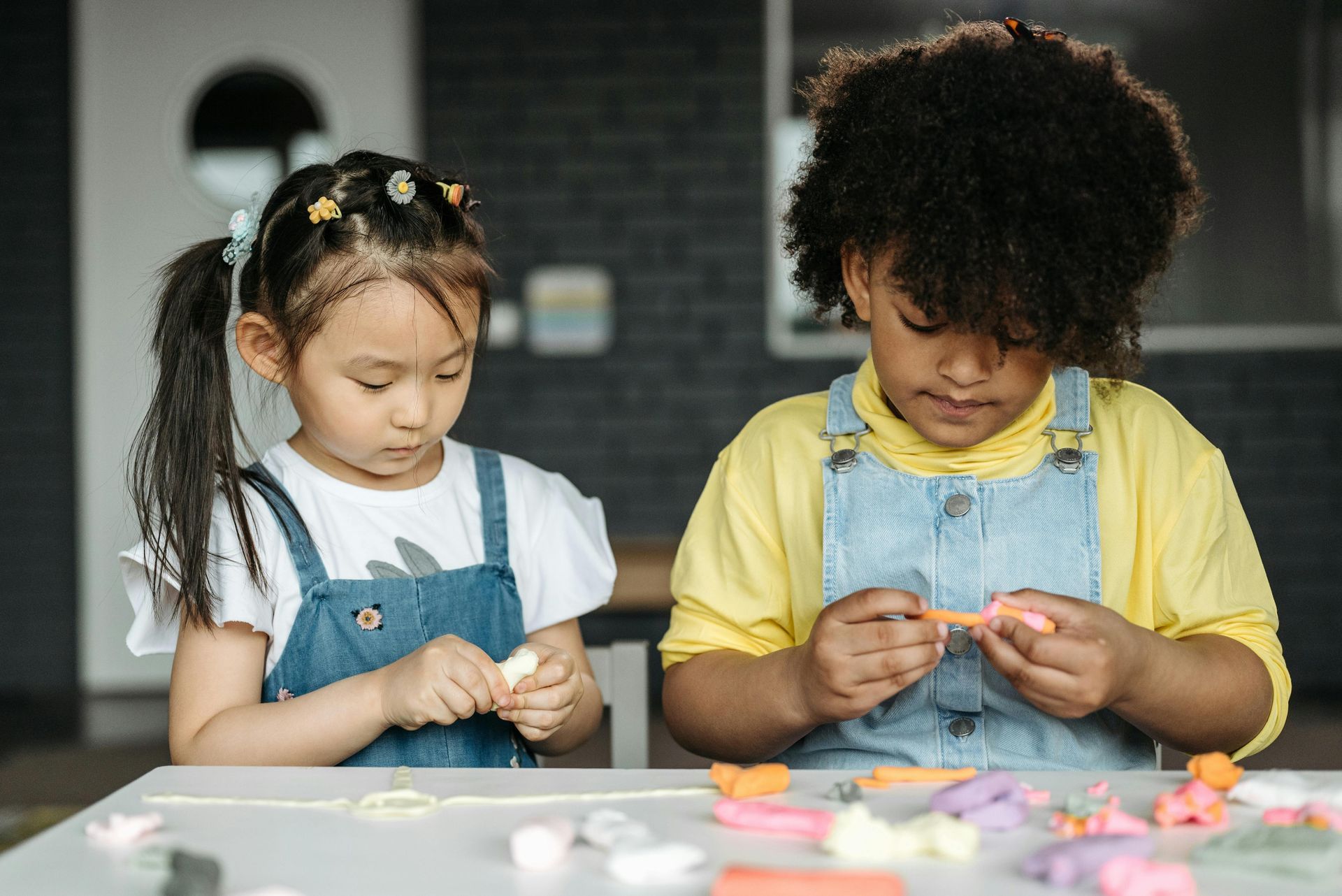 Two children in overalls making crafts at a table with colorful materials
