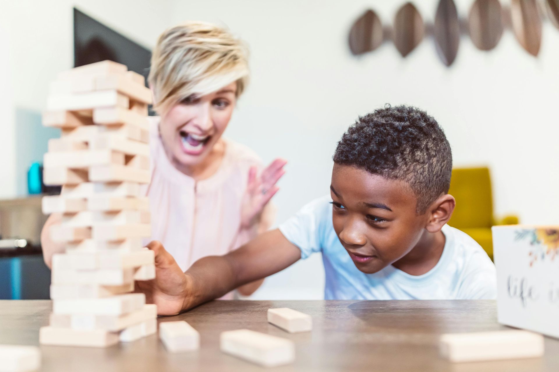 Two people stacking wooden blocks at a table, focused on a tower game indoors