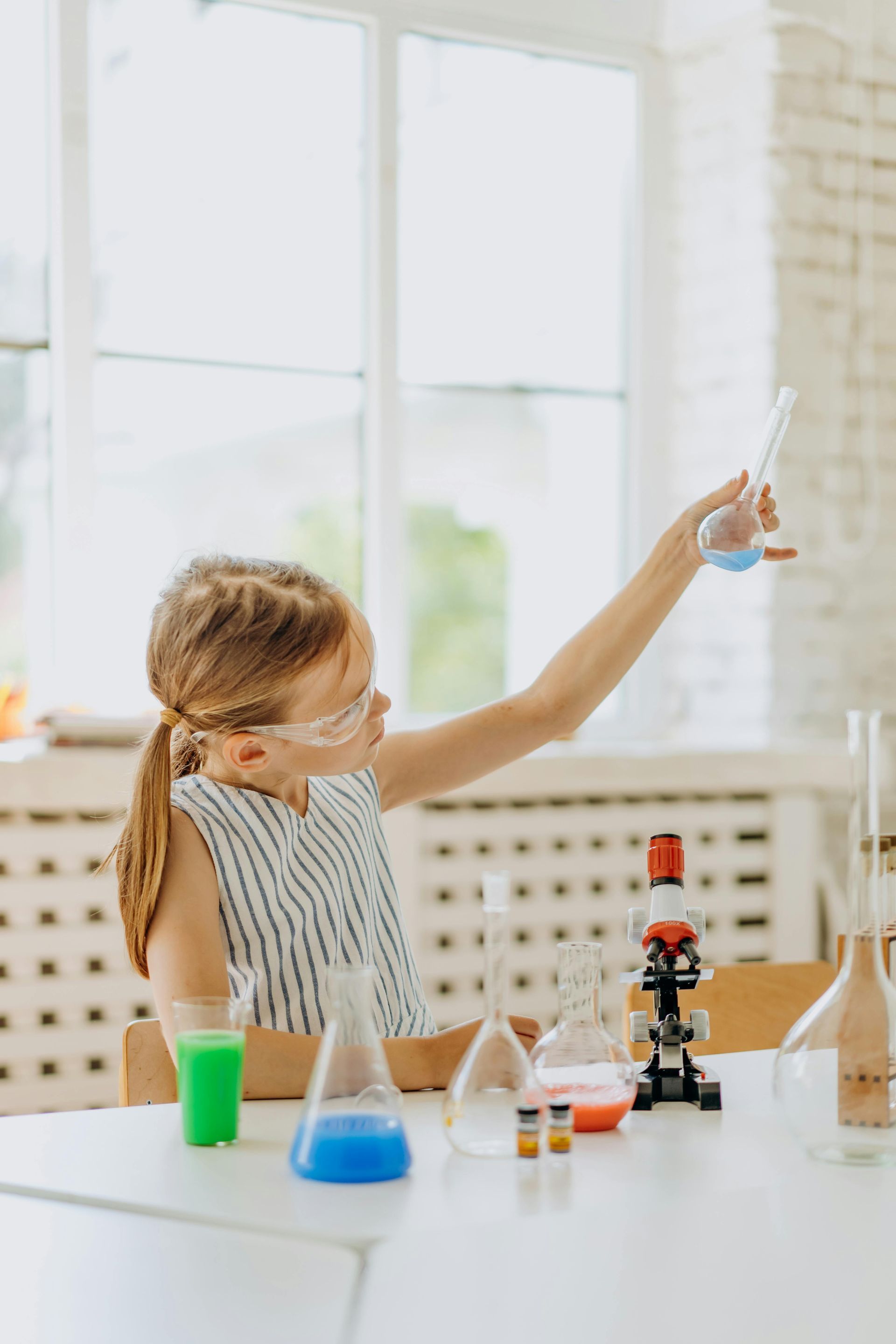 Child doing a science experiment at a table, holding up a dropper with blue liquid and lab tools nearby