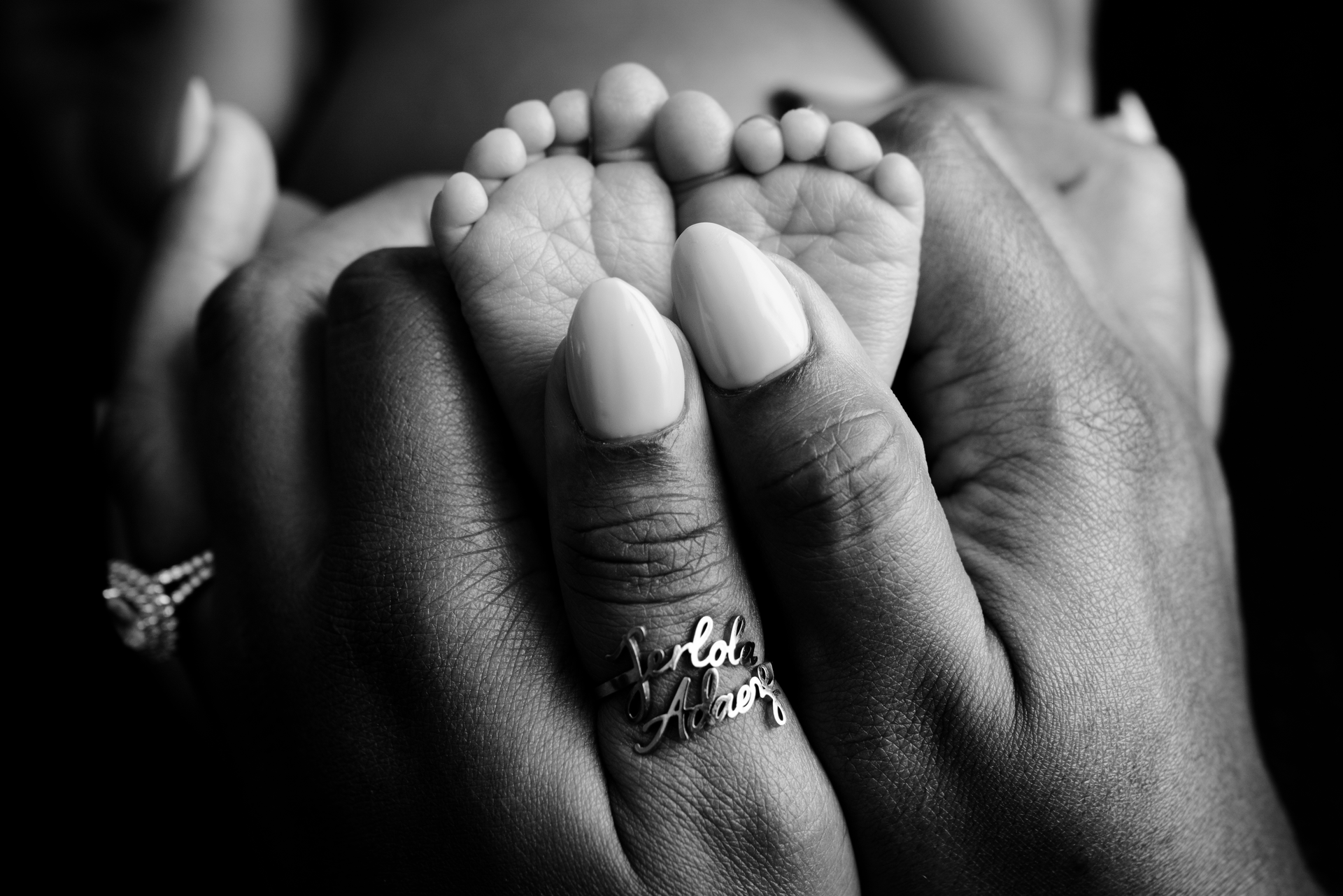 Black-and-white close-up of adult hands gently holding a baby's feet, with a butterfly ring visible.