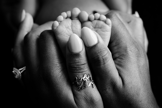 Hands gently holding a baby’s feet in black and white.