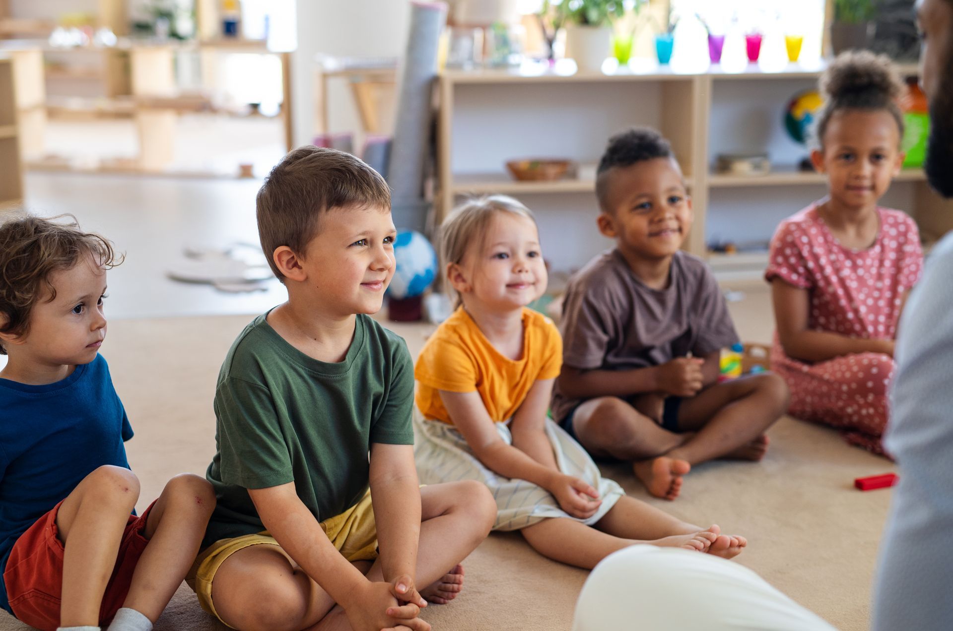 Children sitting on a classroom floor during circle time, listening attentively