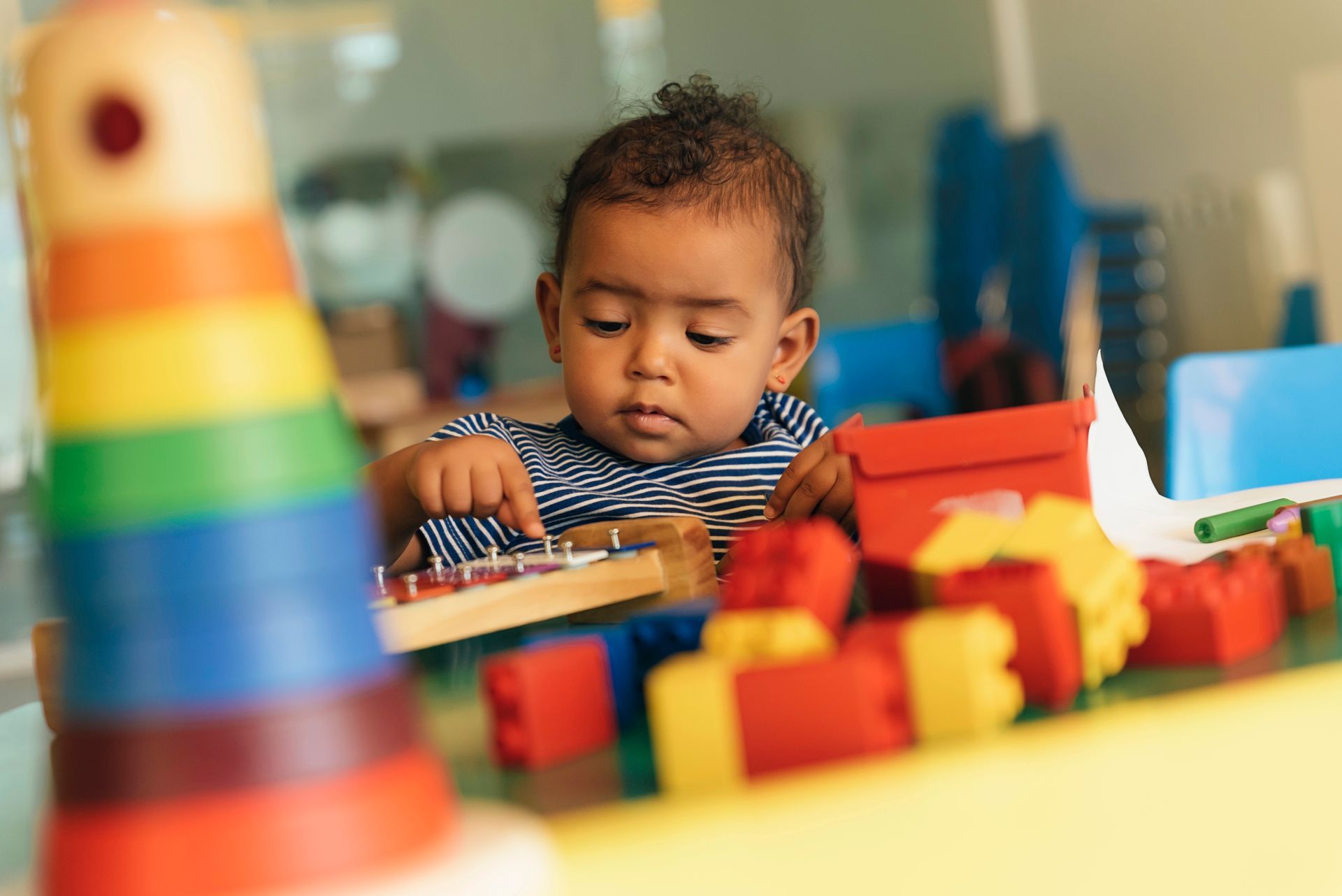 Child playing with colorful toy blocks at a table, focused on building in a bright playroom.