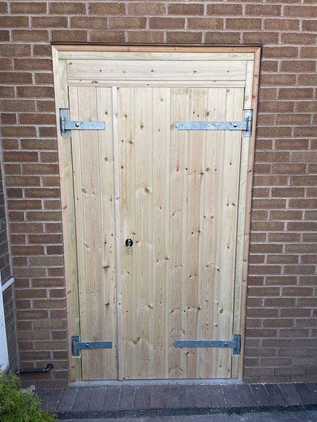 Wide timber garage door with galvanised strap hinges on a brick outbuilding