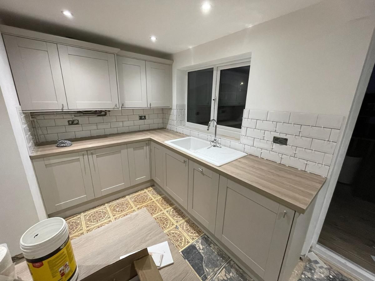 Grey shaker L-shaped kitchen with oak-effect worktops and a white metro tile splashback around the window