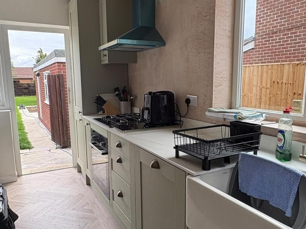 The same Alvaston kitchen after renovation looking toward the back door with sage shaker units, Belfast sink and herringbone flooring