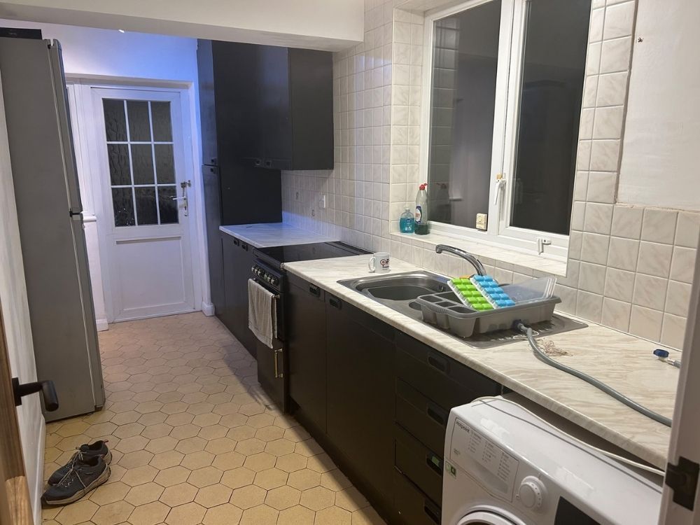 Alvaston galley kitchen before renovation looking toward the back door with black units, stainless sink and dated floor tiles