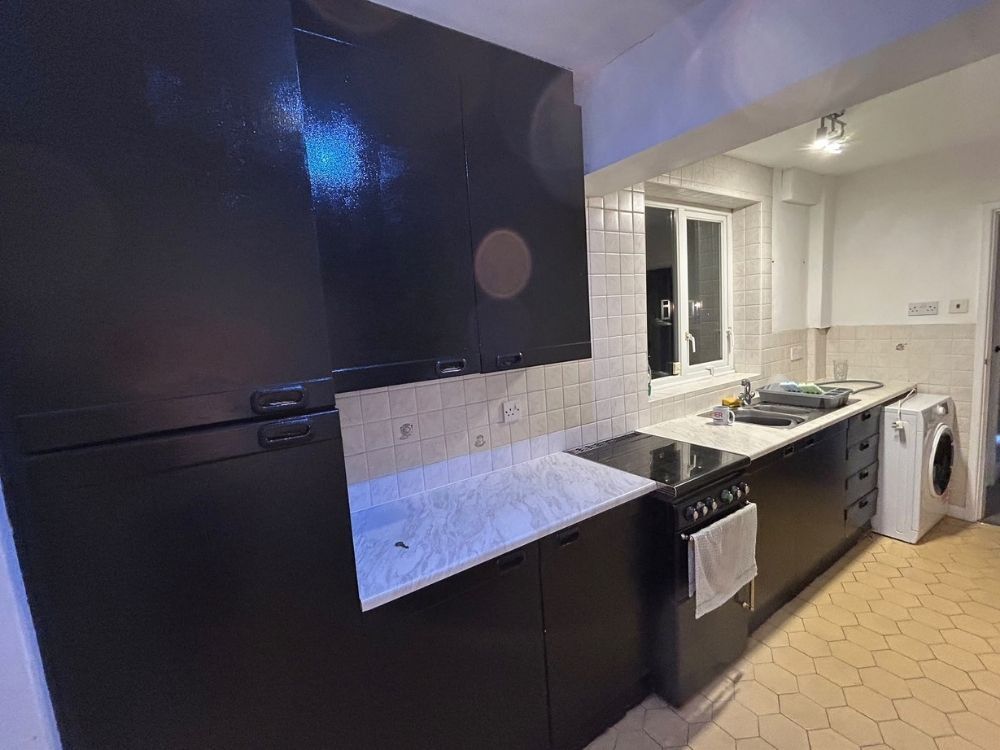 Galley kitchen in an Alvaston home before renovation with high gloss black units, marble effect laminate worktop and tiled walls