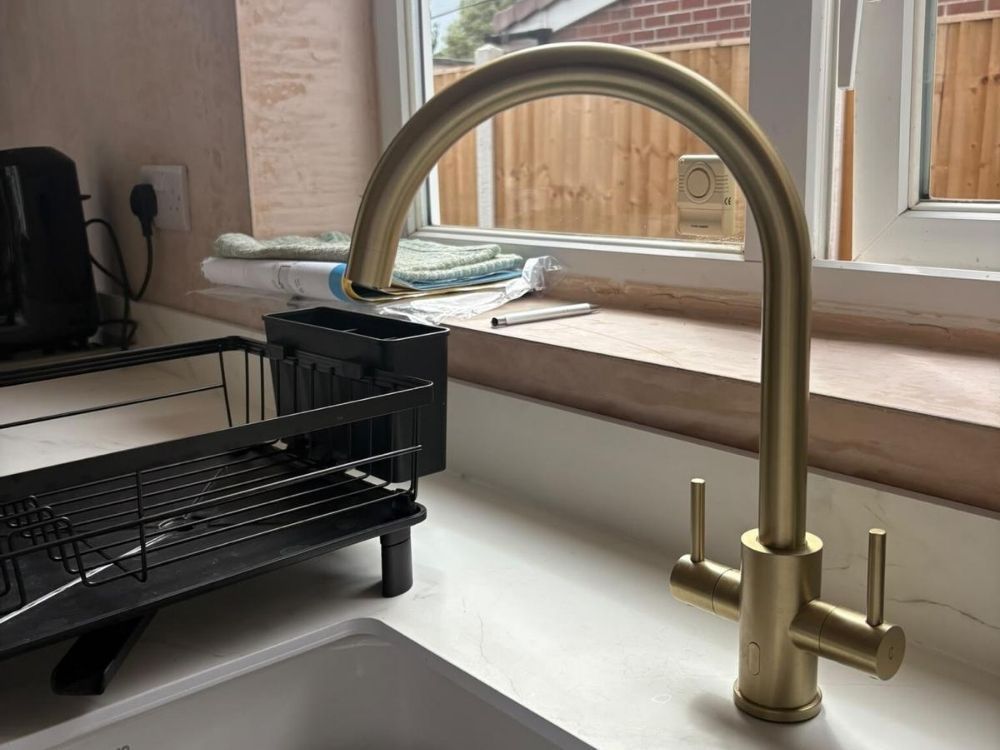 Brushed brass swan neck mixer tap and Belfast sink set into white quartz worktop in an Alvaston kitchen