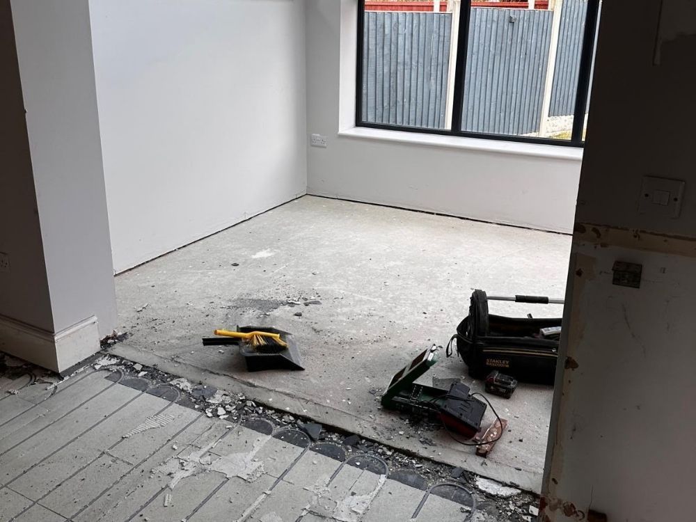 Kitchen stripped back to bare screed during renovation in Spondon with underfloor heating mat visible at the threshold
