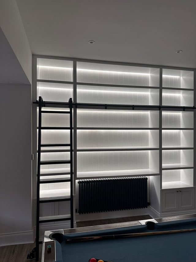 Full-width lit shelving wall with base cupboards in a games room