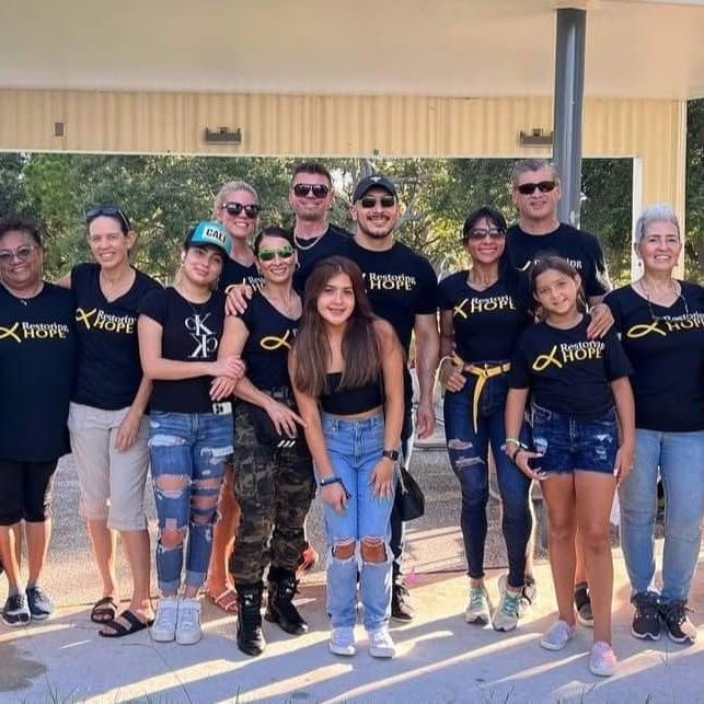 Group of people posing outdoors in matching black shirts, standing in front of a building.