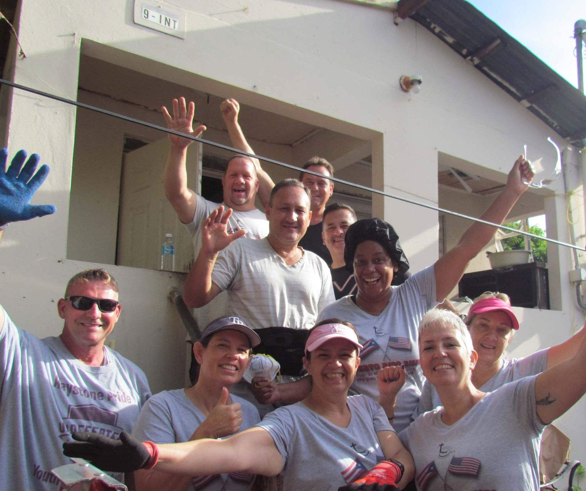 Group of smiling people waving outdoors in front of a building