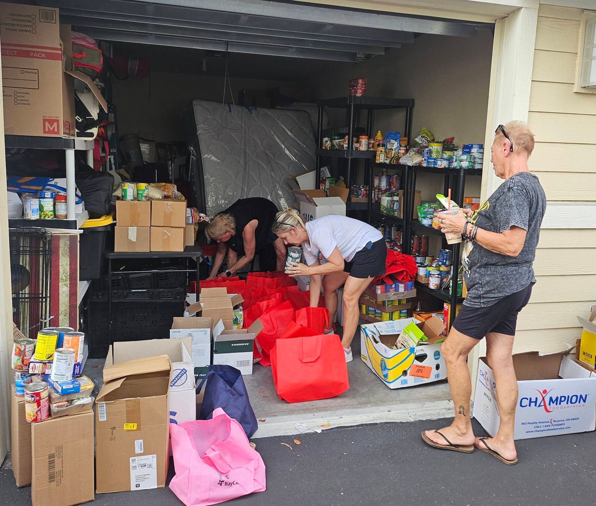 Volunteers sorting donated supplies in a garage, with boxes, bags, and shelves of food items.
