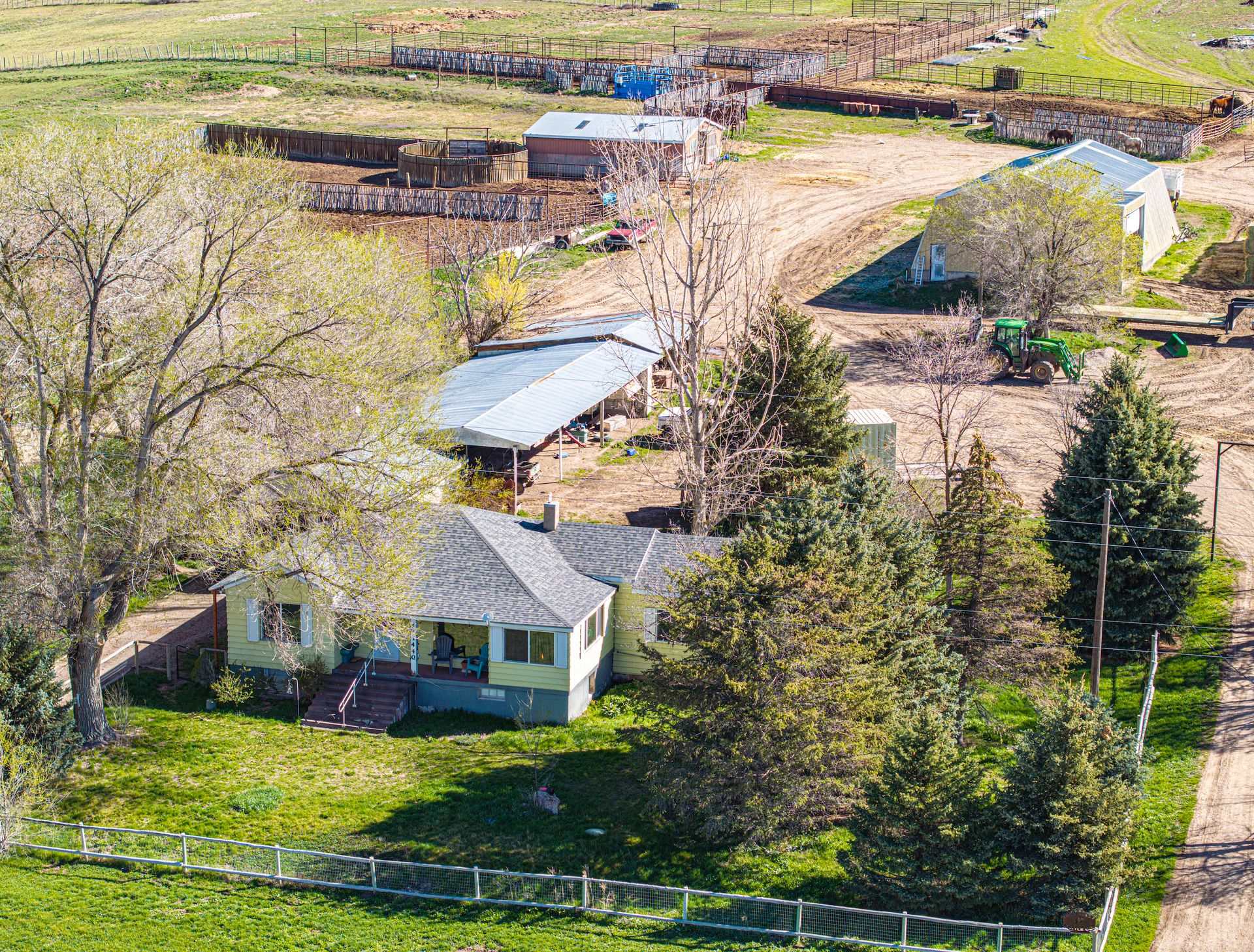 Aerial view of a farmhouse, outbuildings, and fenced fields in a rural landscape