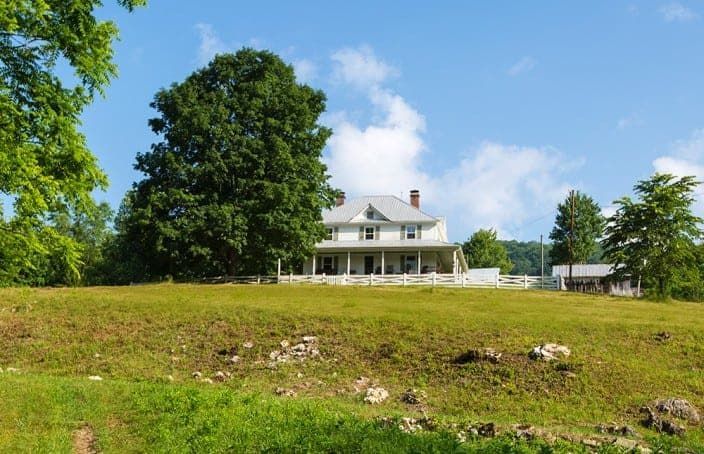 A large white house sits in the middle of a grassy field.