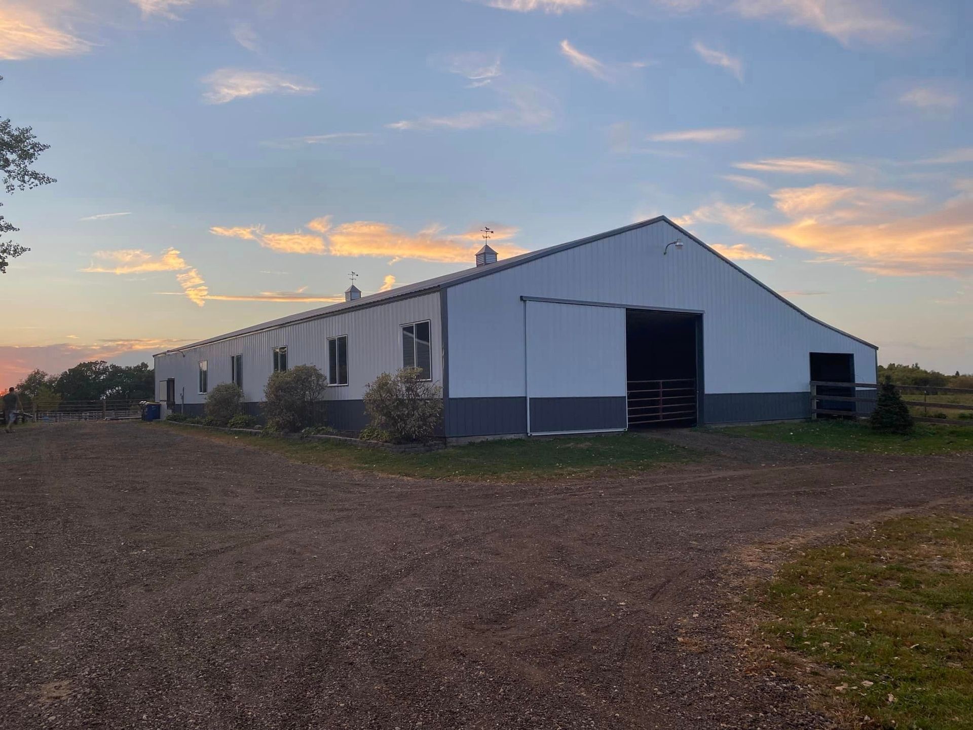 A large white barn is sitting in the middle of a dirt field.