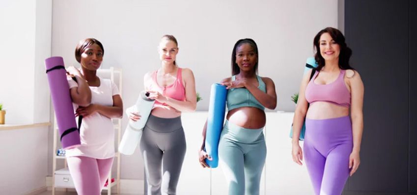 Four people in workout clothes holding yoga mats stand in a bright studio.