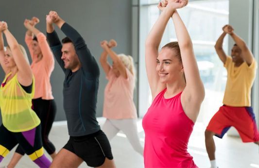 People doing a group fitness class with arms raised in a bright studio
