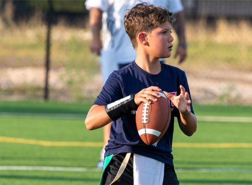 Boy holding a football on a grassy field, looking to the side during practice.