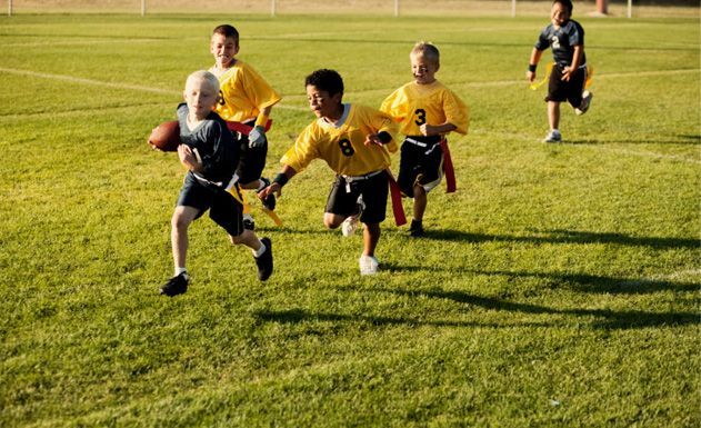 Children playing soccer on a sunny grassy field, chasing the ball during a match