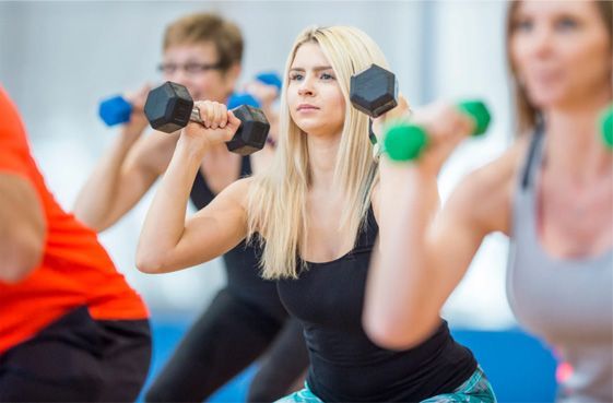 People exercising with dumbbells in a fitness class, with a blonde woman centered in focus