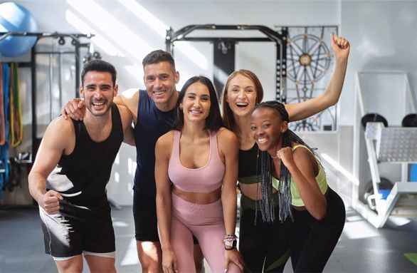 Four people posing and smiling in a gym with workout equipment in the background